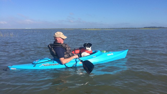 A man and a dog in a kayak surrounded by water. 