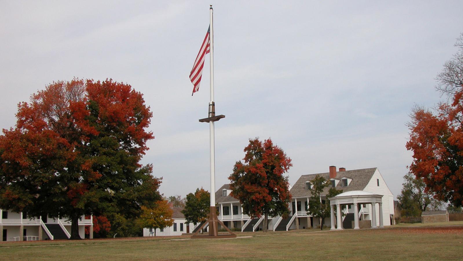 The grassy parade ground with trees, American flag flying on the flagpole, and officer's quarters.