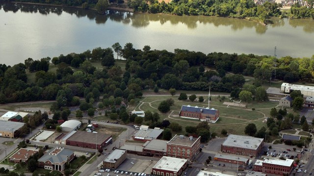 An aerial photo showing the park grounds with dark trees and the Arkansas River.