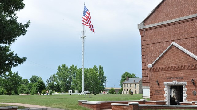 The entrance to the red brick visitor center stands in front of the flagpole and commissary building