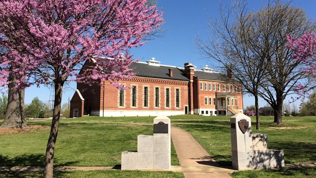 Blooming Redbud trees frame a sidewalk leading to the three-story red brick visitor center.