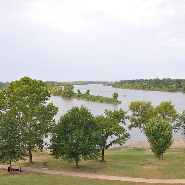 The confluence of the Arkansas and Poteau Rivers with green trees and grass on the banks.