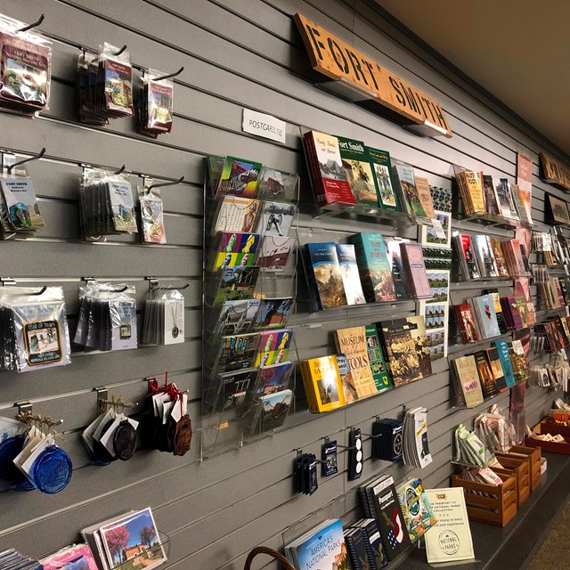 The gray wall of the bookstore displaying books, pins, patches, ornaments, and other souvenir items.
