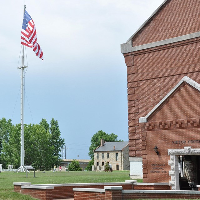 The entrance to the red brick visitor center stands in front of the flagpole and commissary building