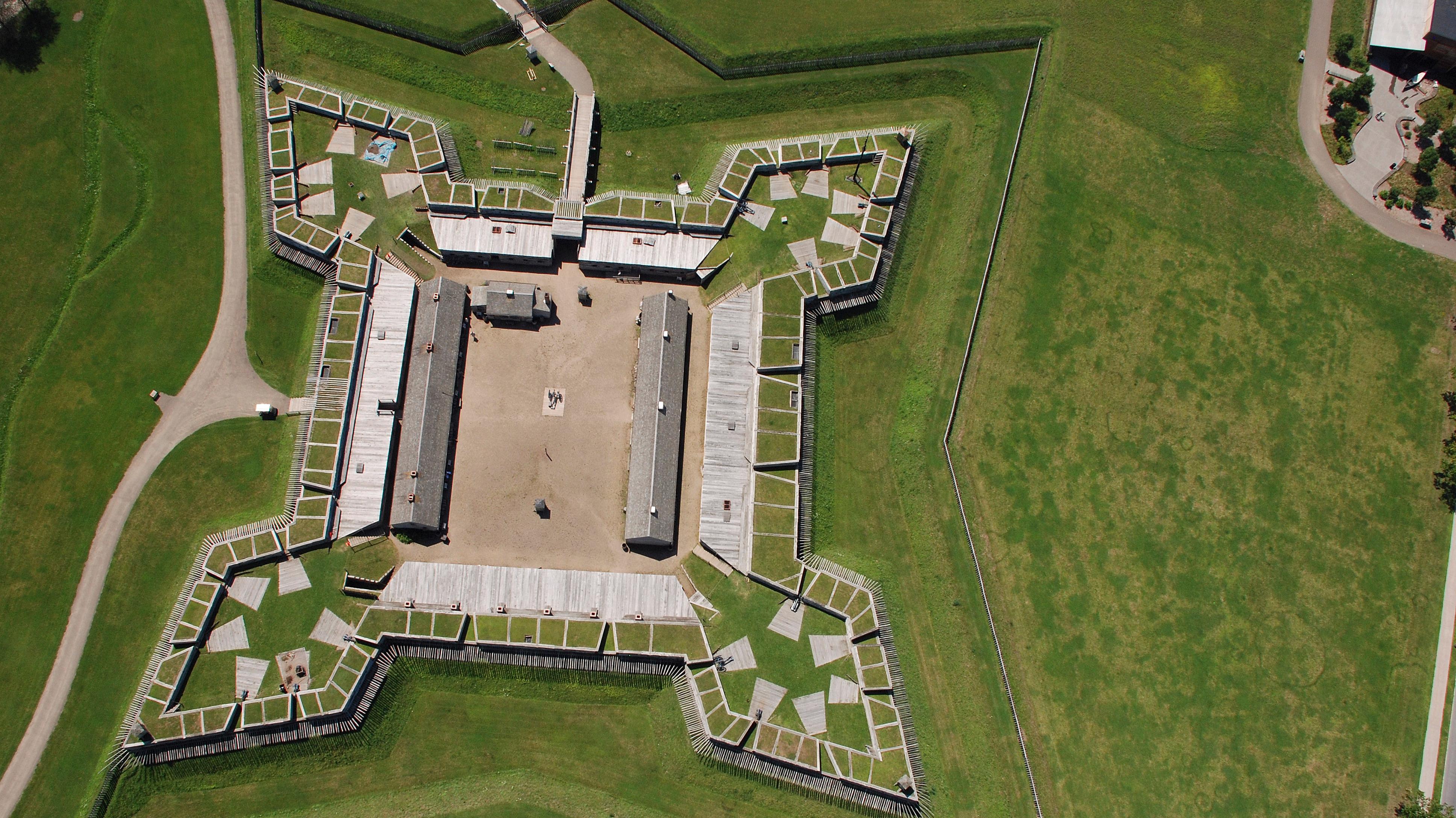 A view of the fort from above. A wooden star-shaped building sits in the middle of a grass field.