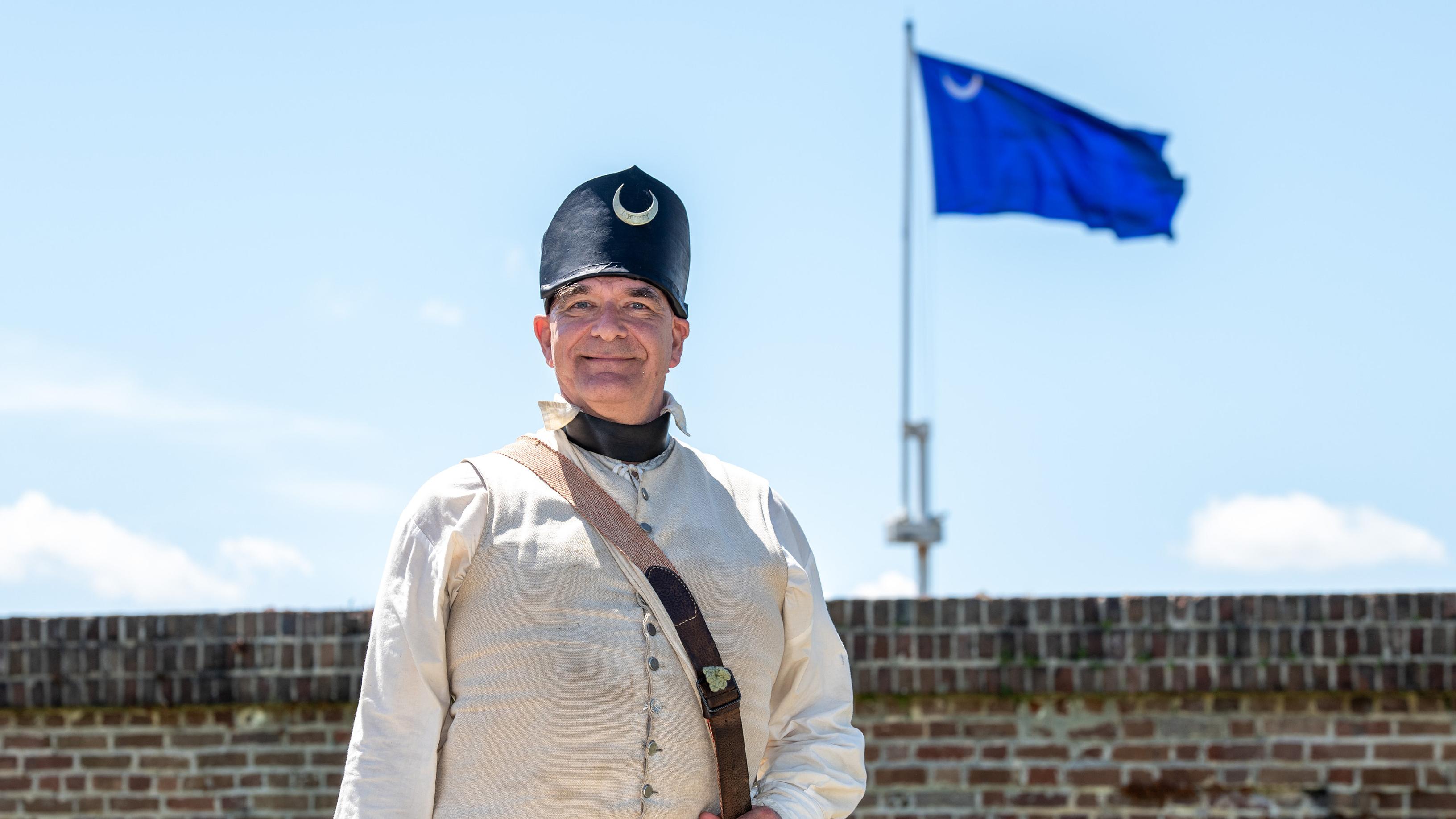 An American Revolution living historian in a period uniform stands in front of Fort Moultrie.