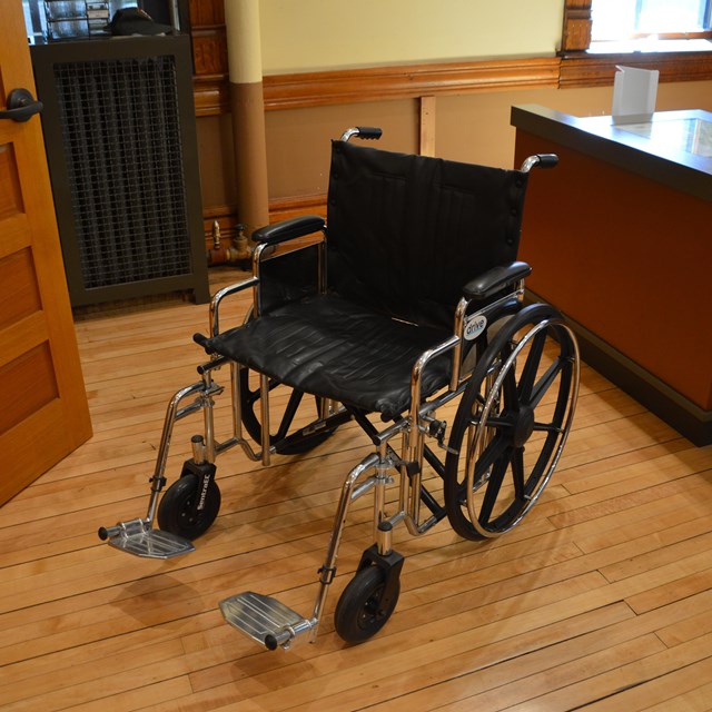 An empty wheelchair in a room with a long desk in the background.