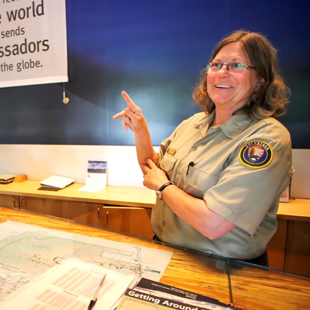 A person wearing an NPS volunteer uniform making a k-shape in American Sign Language.