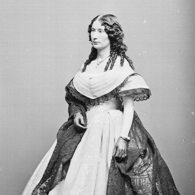 Laura Keene, a white woman in her 30s with dark hair with curls and wearing a large hooped dress.