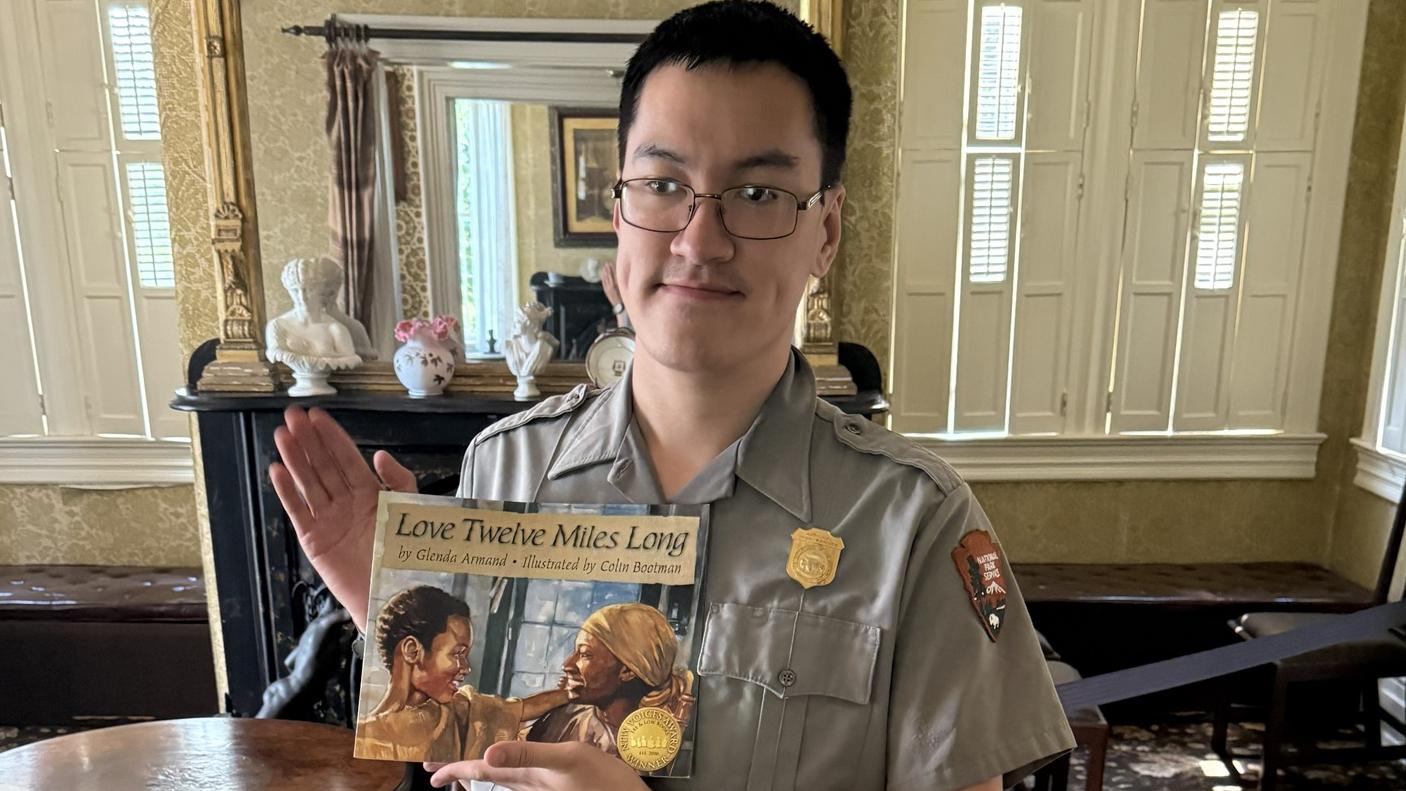 NPS Ranger stands in well-furnished room holding a book