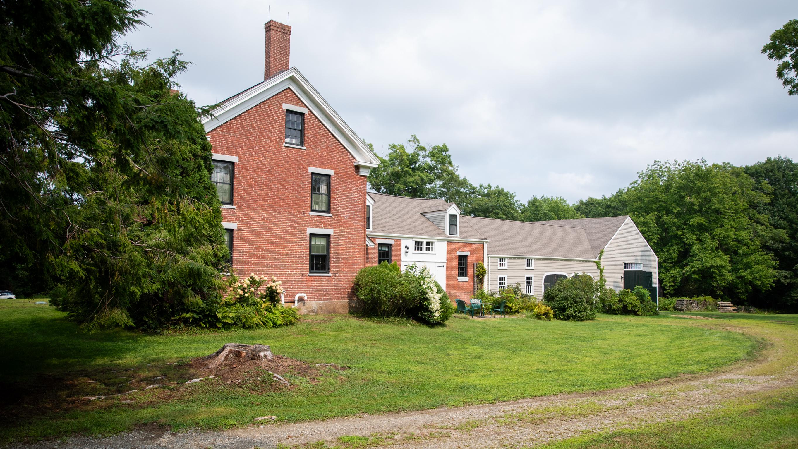 A gravel roadway bends towards the red brick and grey clapboard house.
