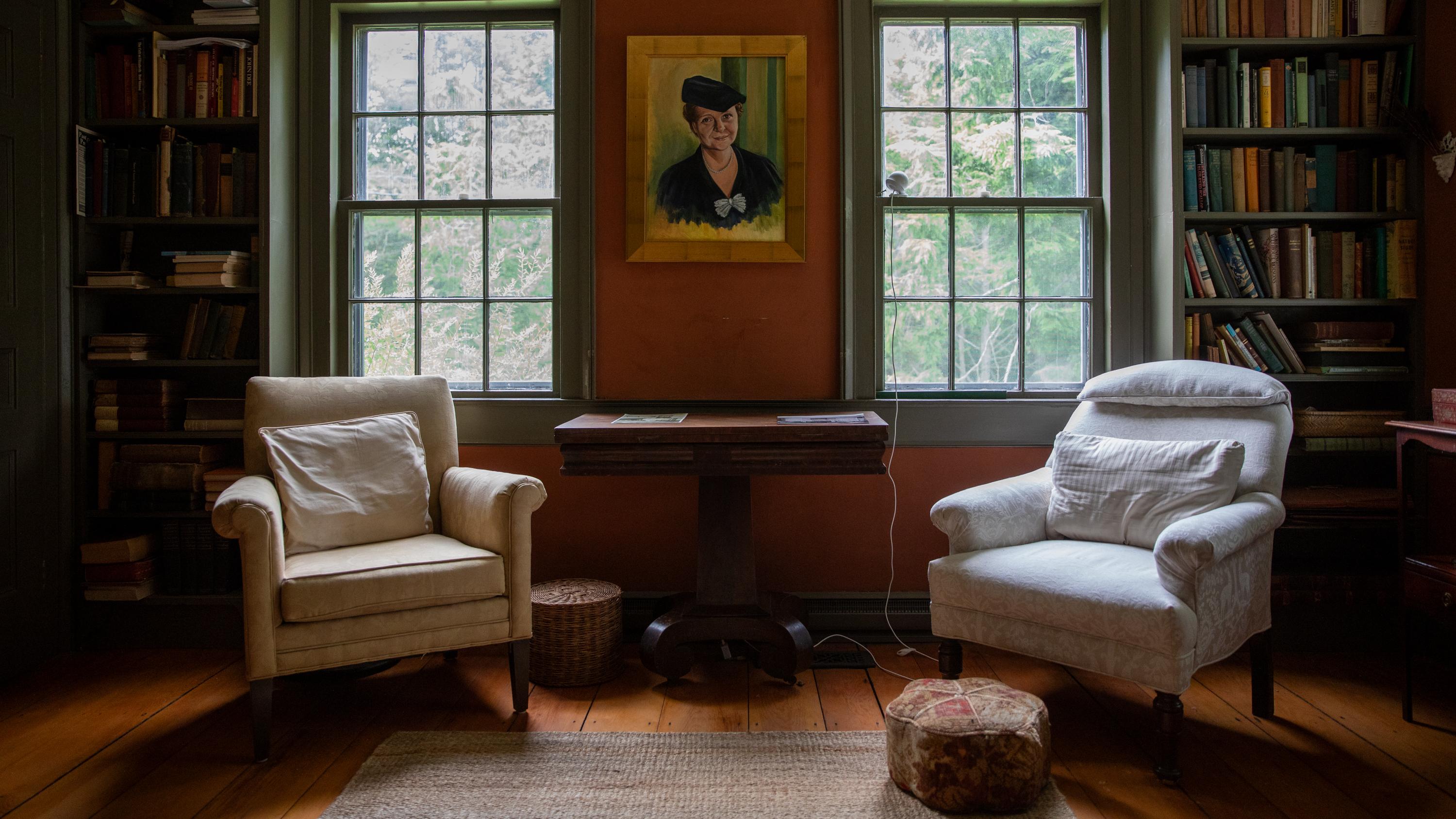 Two white chairs centered between two windows in a red room with full bookshelves.