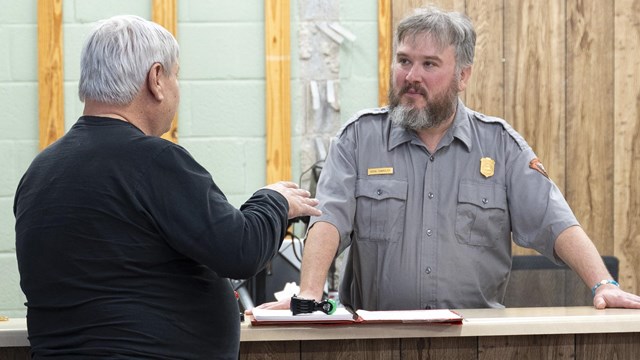 A ranger talking to a visitor at a visitor center desk.