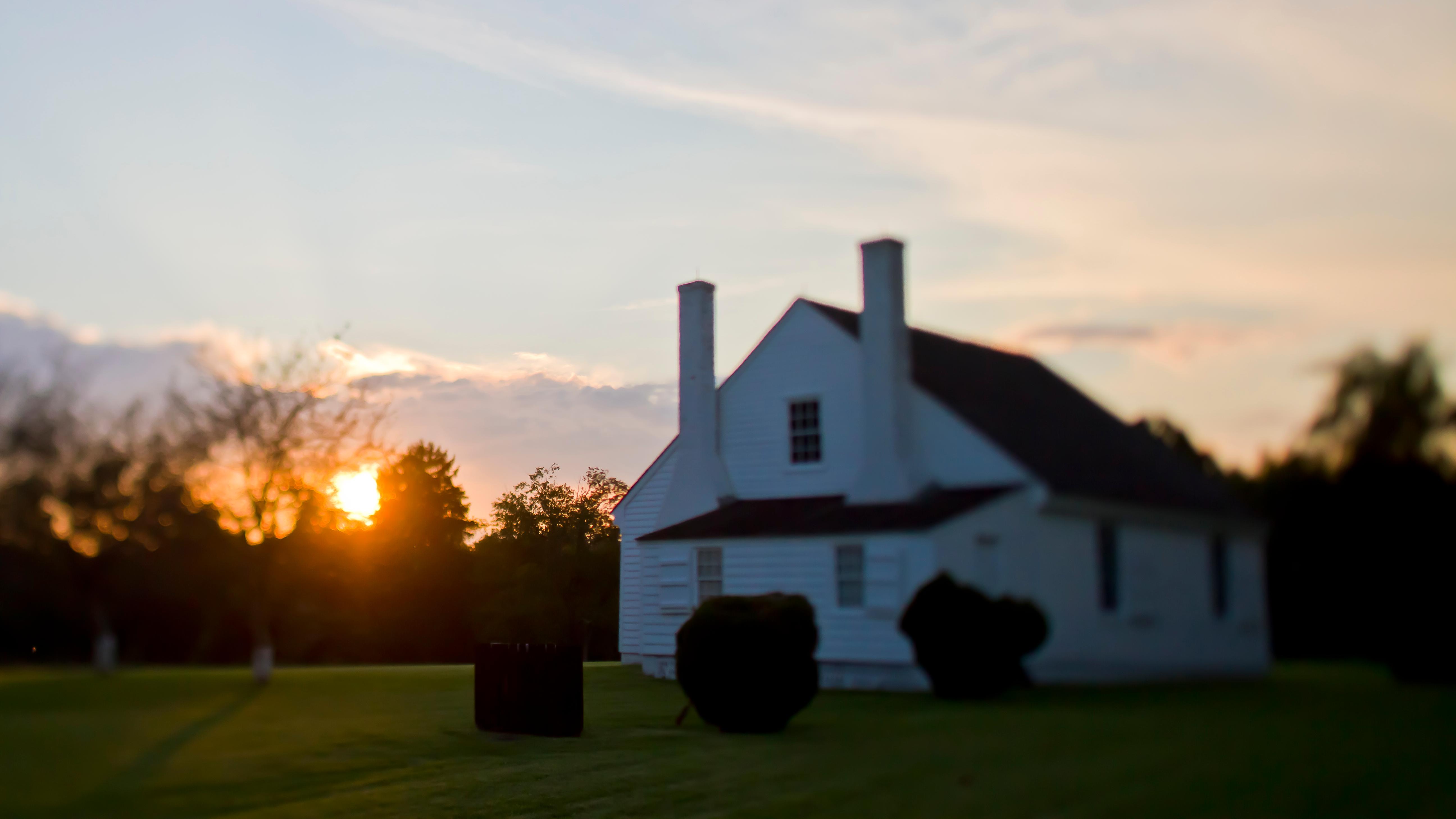 A small, white house with a-frame roof at sunset.