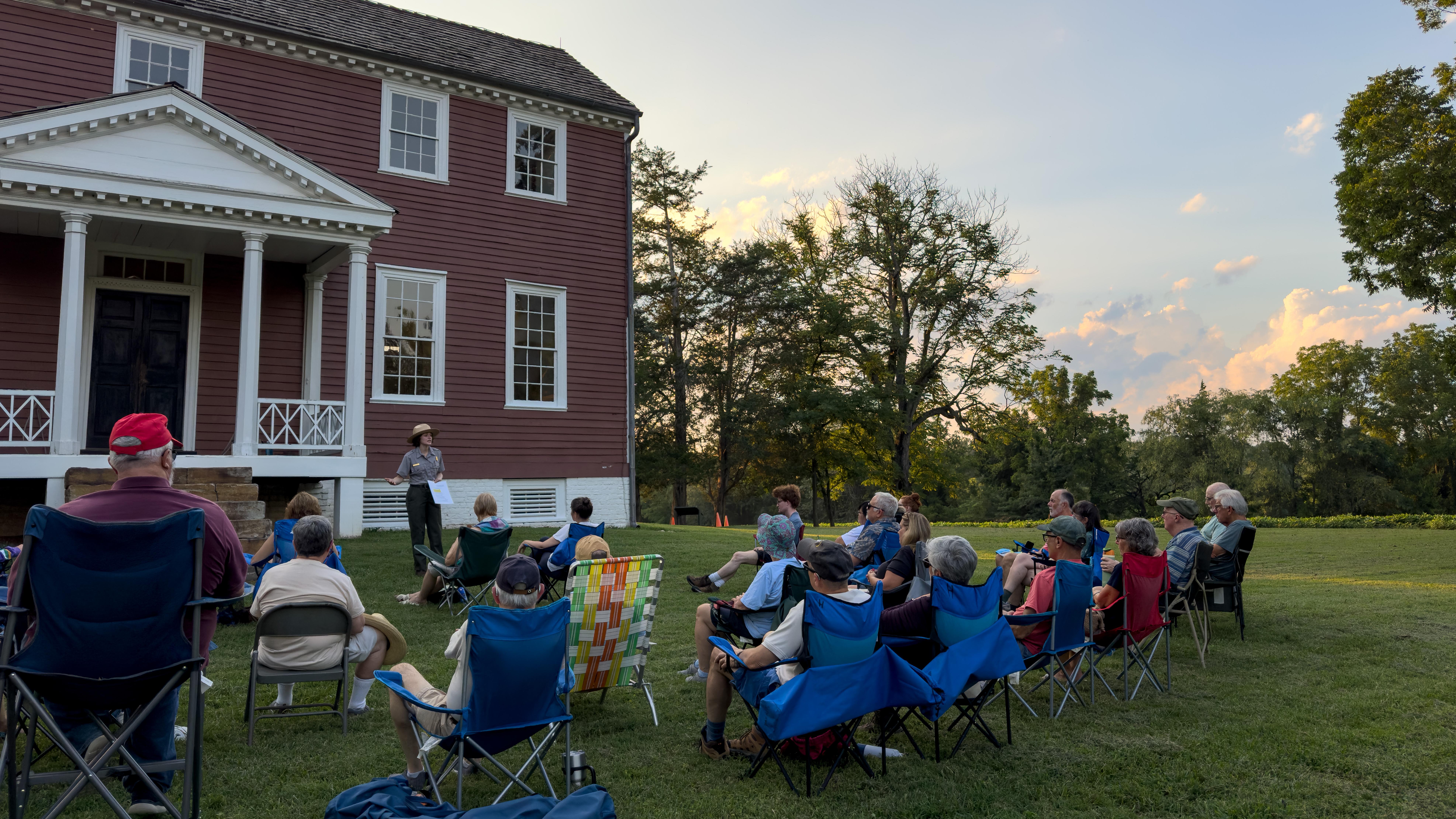 A ranger speaks to people on a lawn outside a historic house.