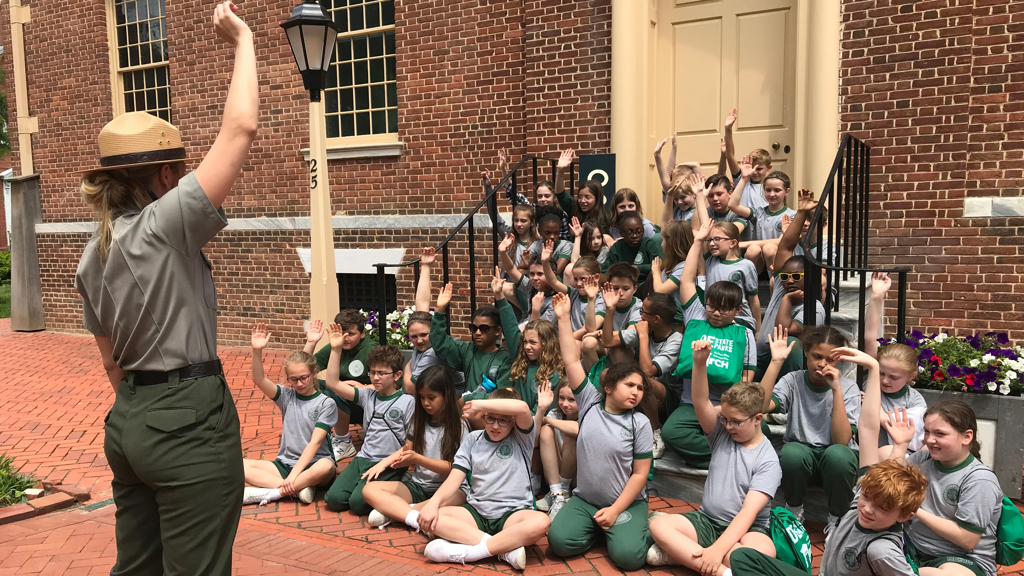Children sitting in a large group being sworn in as Junior Rangers by a NPS Park Ranger.