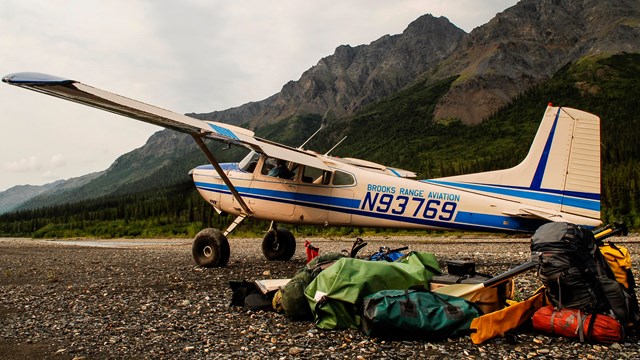 A bushplane drops off a load of gear and people on a river bar in the mountains