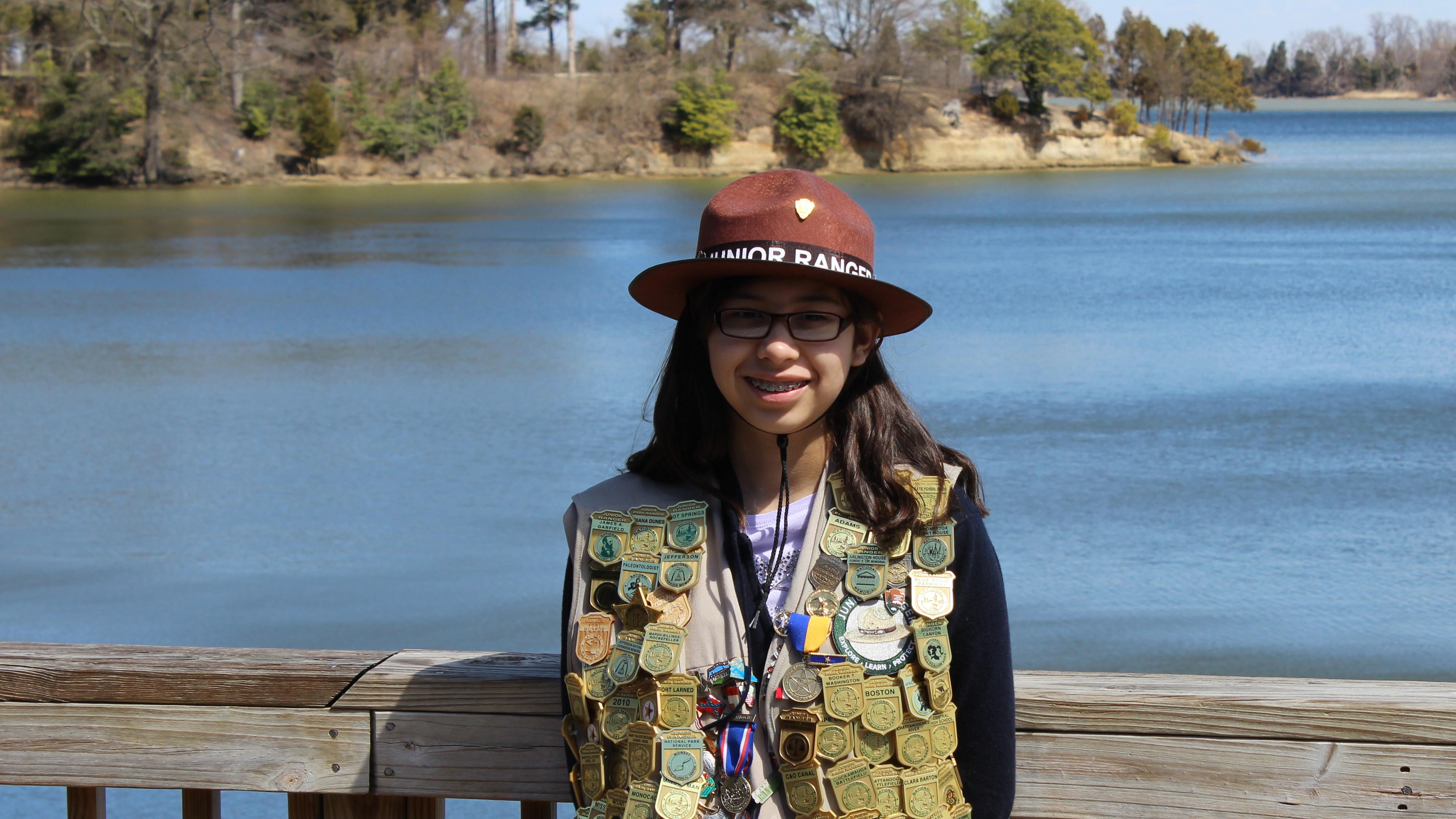 Junior Ranger with vest of badges standing on deck overlooking Popes Creek
