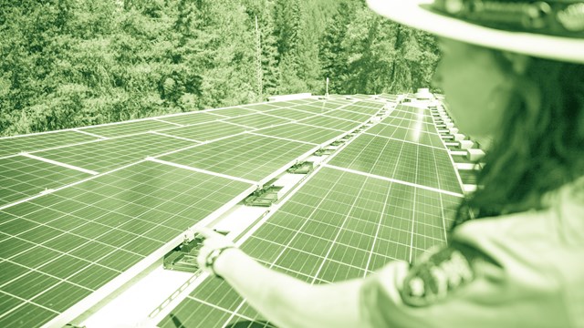 A park ranger points to solar panels. 