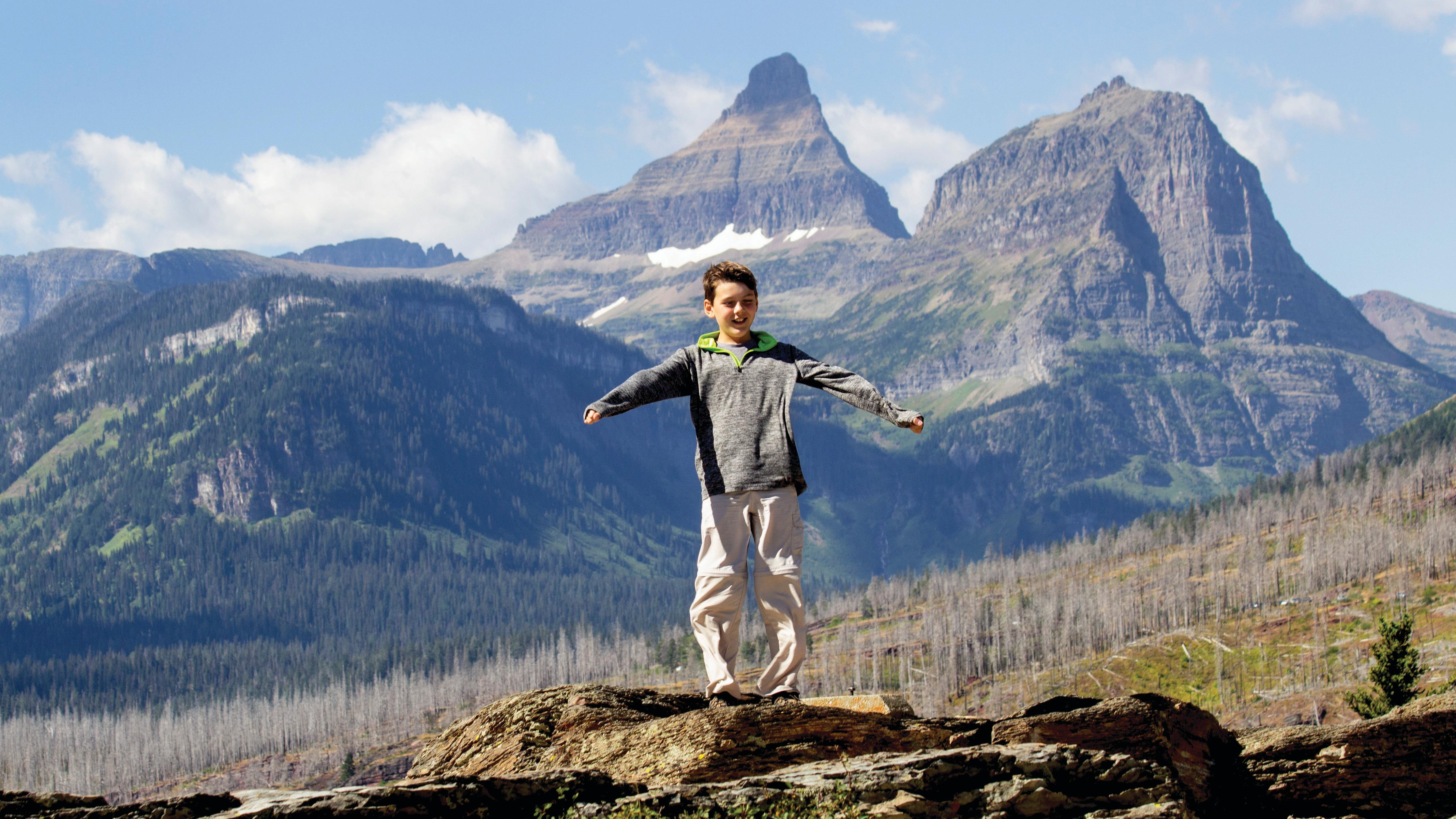 A young boy stands on a rock with the wind whipping at his clothes.