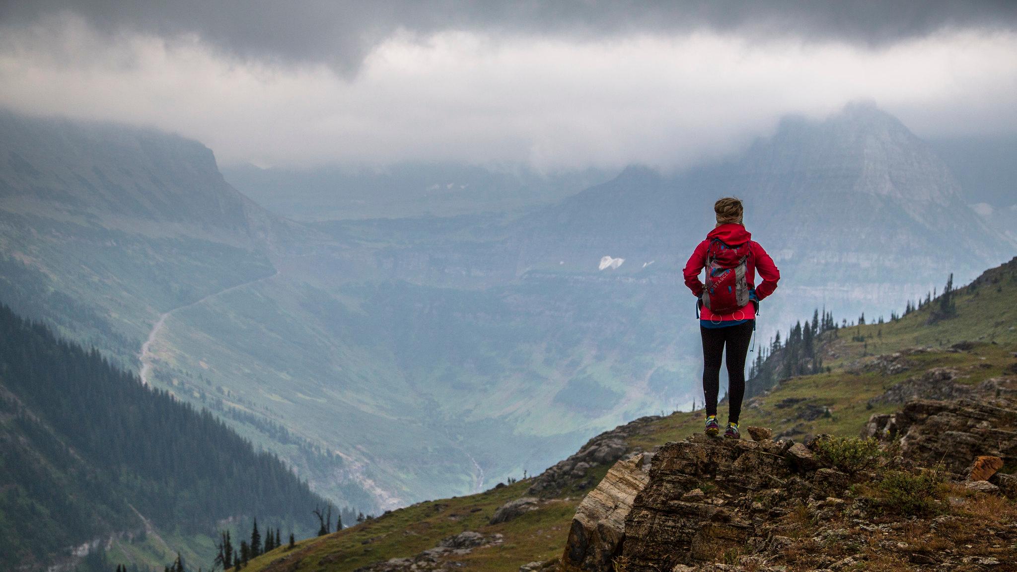 A hiker stands on a rock in the mountains with a vast landscape beyond. 
