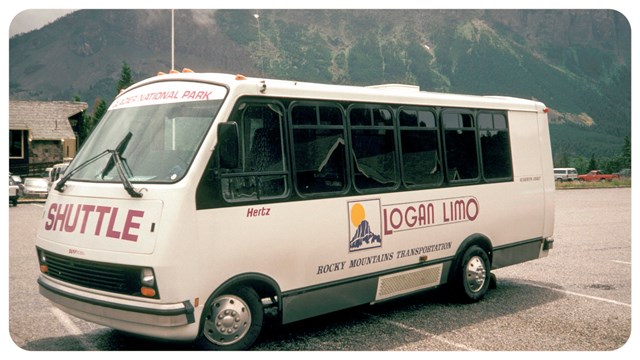 A red bus parked on a mountain road with peaks in the background