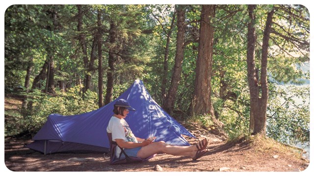 a person sitting by a tent in the forest