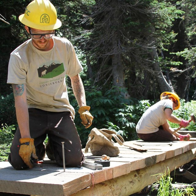 Trail workers in Conservancy t-shirt work on wood bridge