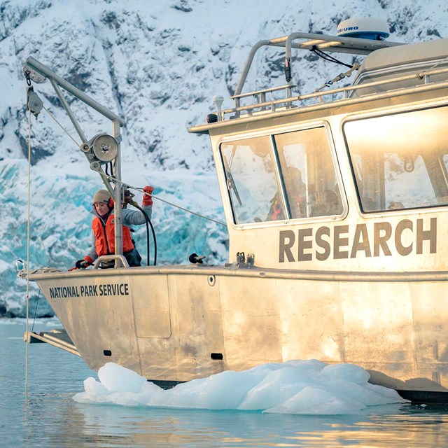 A park ranger works a rope pulley device on a research boat in front of Margerie Glacier
