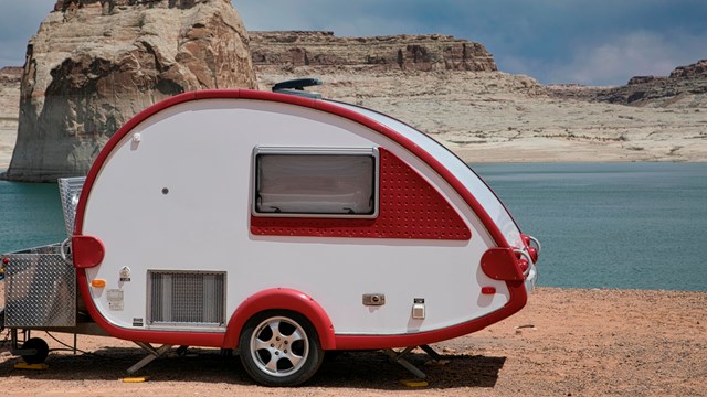 Teardrop camper parked on on a beach at a desert lake. Large sandstone rock formations in background