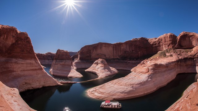 A houseboat winds through high sandstone cliffs on a desert lake.