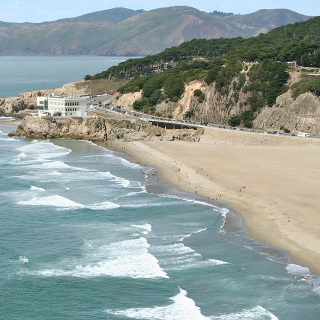 Expansive view of a sandy beach with a white building and mountains in the background.