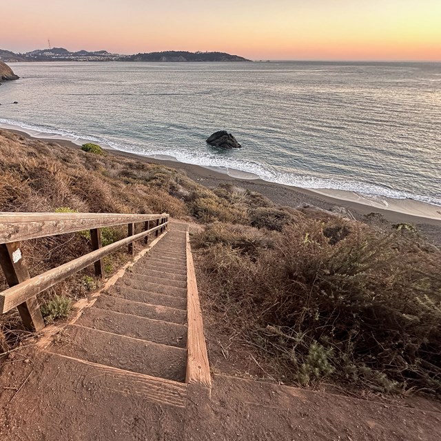 Wooden stairs descend toward a beach at sunset