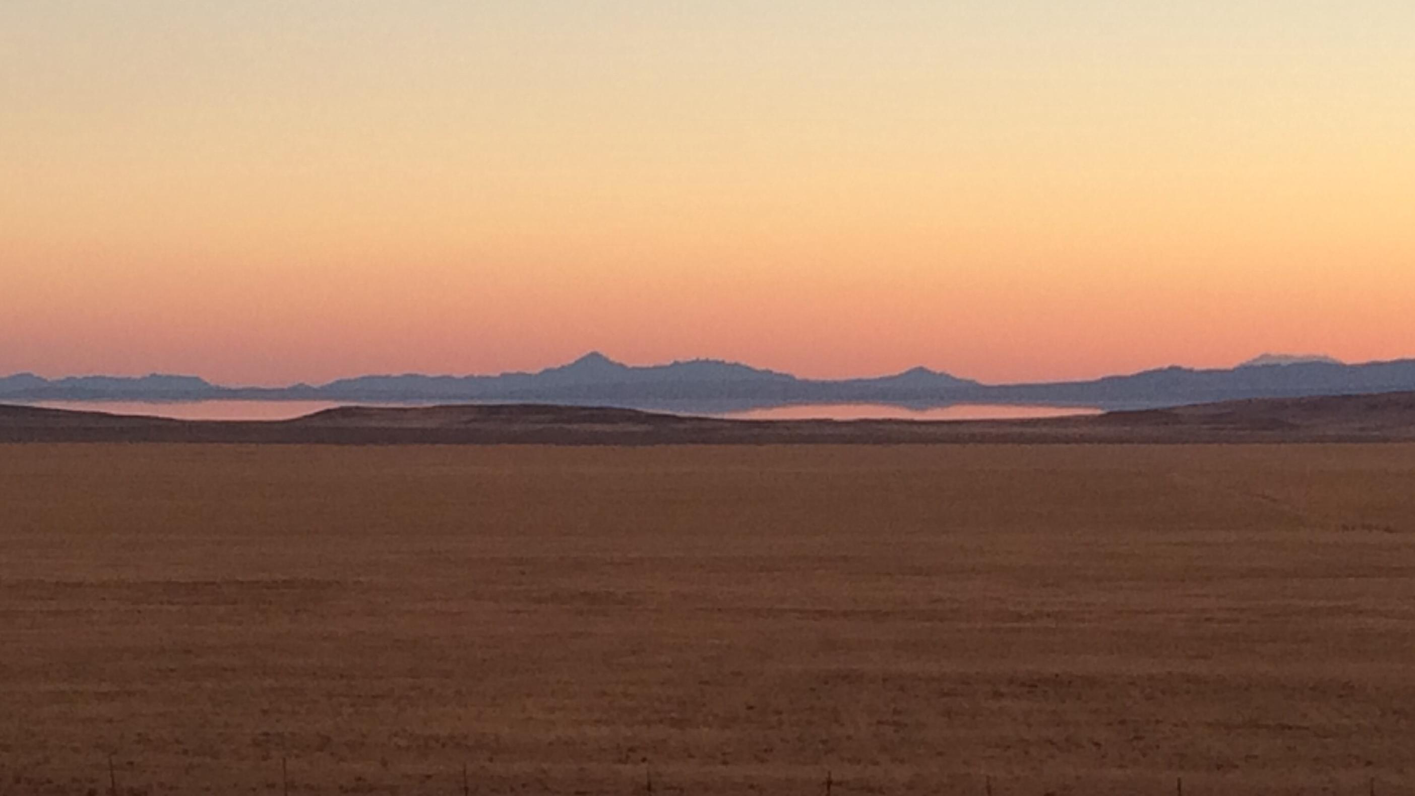 An orange and pink sky meet the top of distant mountains with the Great Salt Lake in the foreground.