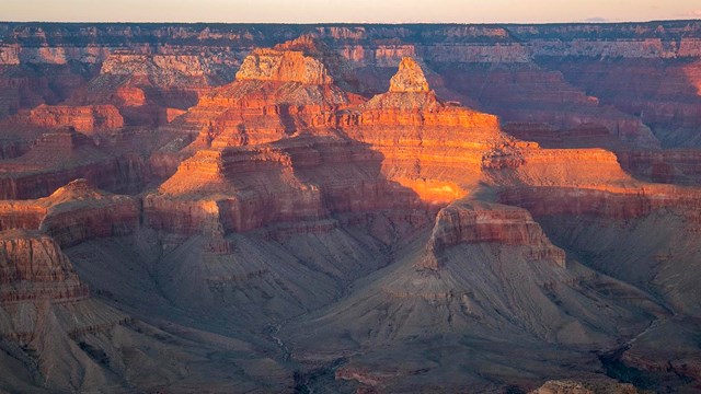 the last warm light of sunset falling onto the tops of peaks within a vast canyon landscape 