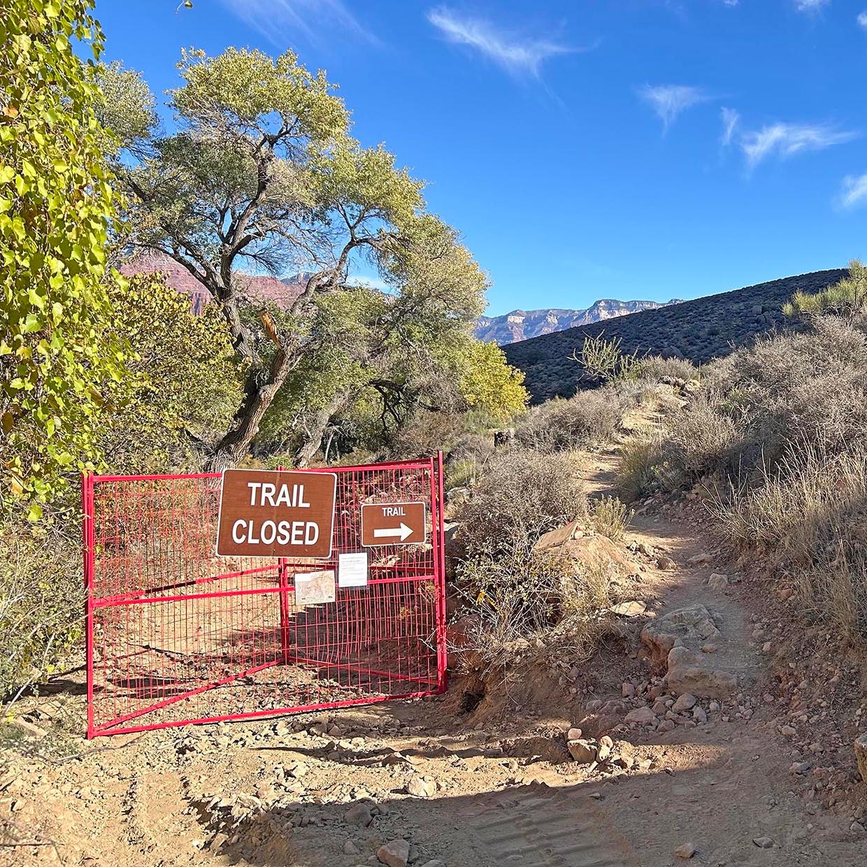 On a backcountry trail. an orange gate with a sign that reads, 