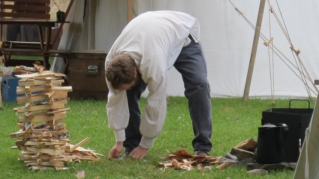 A man bent over a pile of wood kindling.