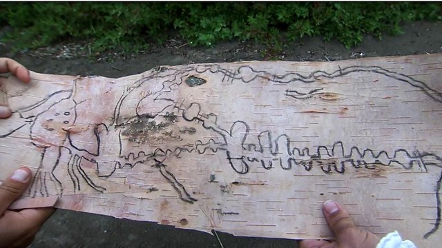 Hands holding a charcoal drawing of a map on birchbark.