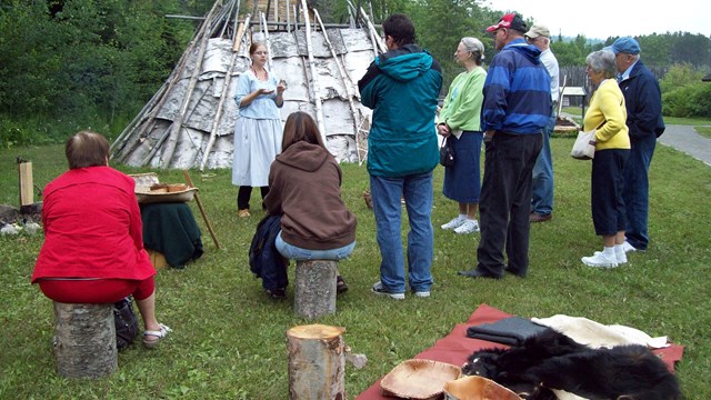 A costumed interpreter gives a program outdoors to a group of visitors.