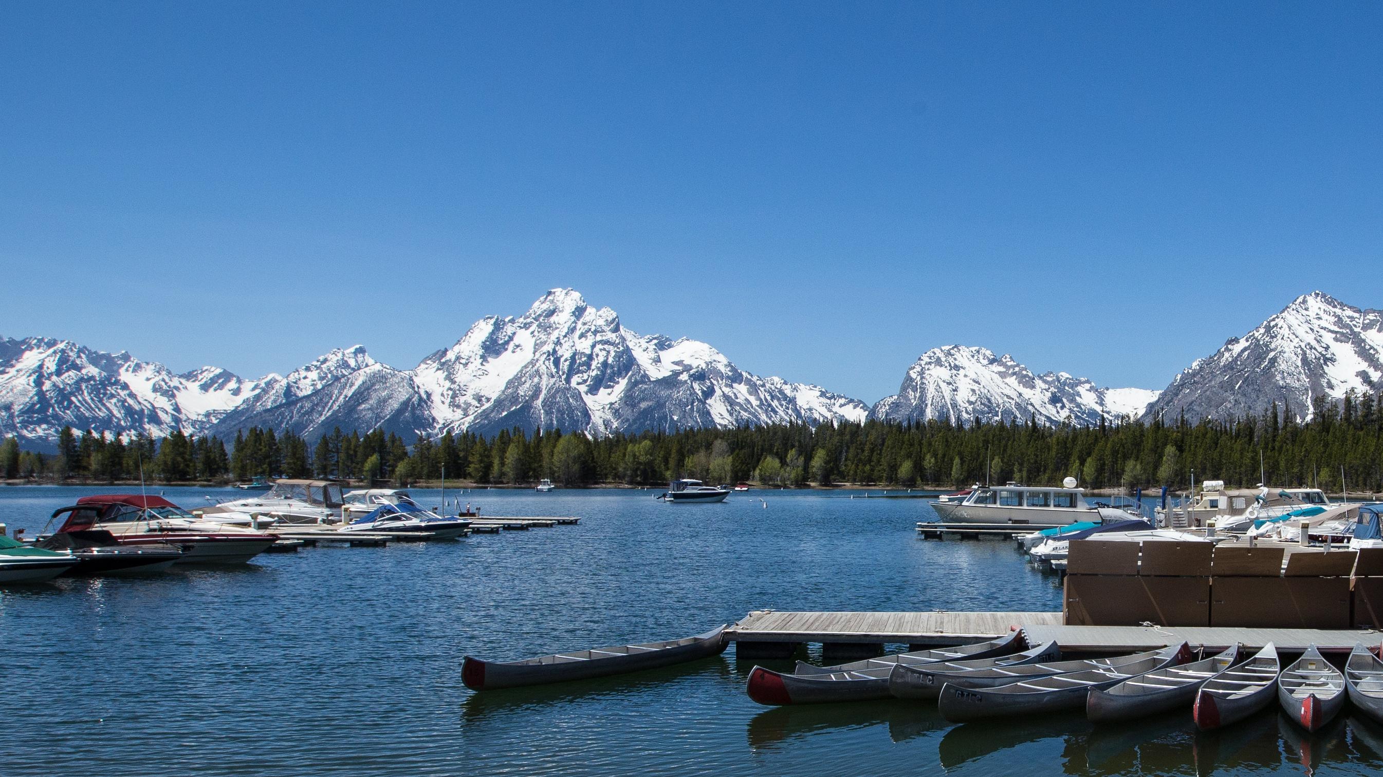Boats tied up to docks in calm bay with the snowcapped Tetons peaks in the distance