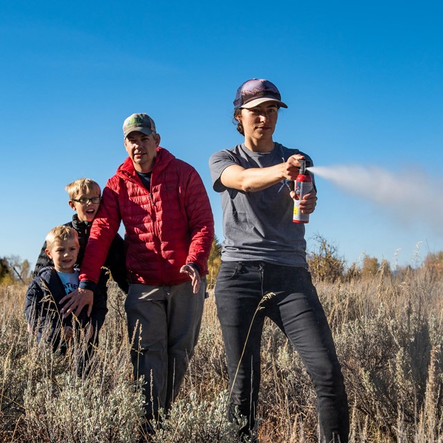 a woman sprays bear spray while a man with two kids stands behind