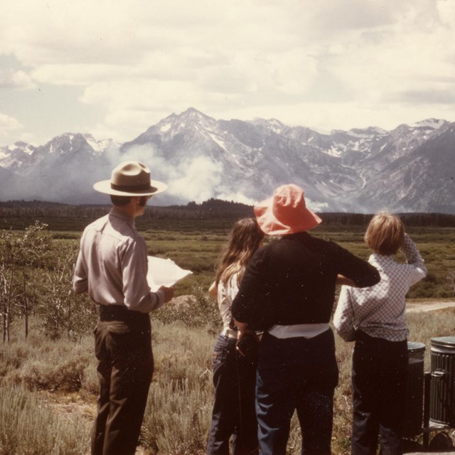 A ranger talks with three visitors about the wildfire in the distance.