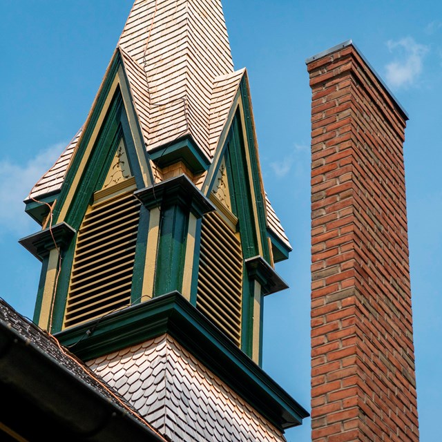 A church steeple, painted in green and yellow, along with a brick chimney.