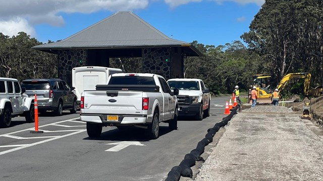 Road leading to a small building with construction materials, road cones, and trucks