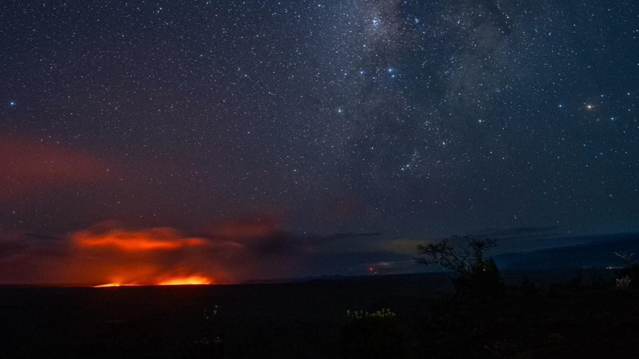 A glow from volcanic activity at night with the milky way above it. 