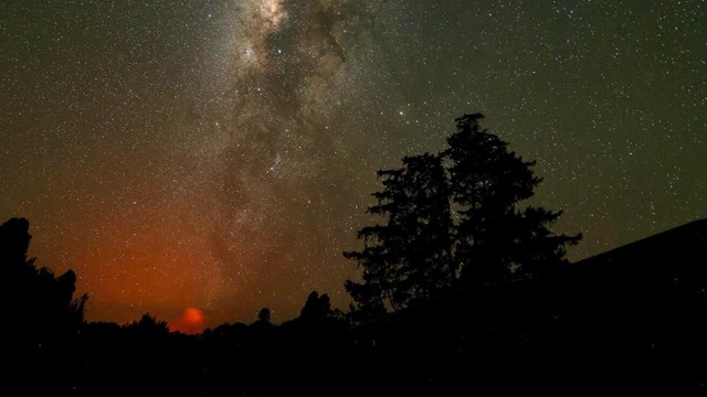 Milky way and glow from a volcanic eruption can be seen in a distance at night. 