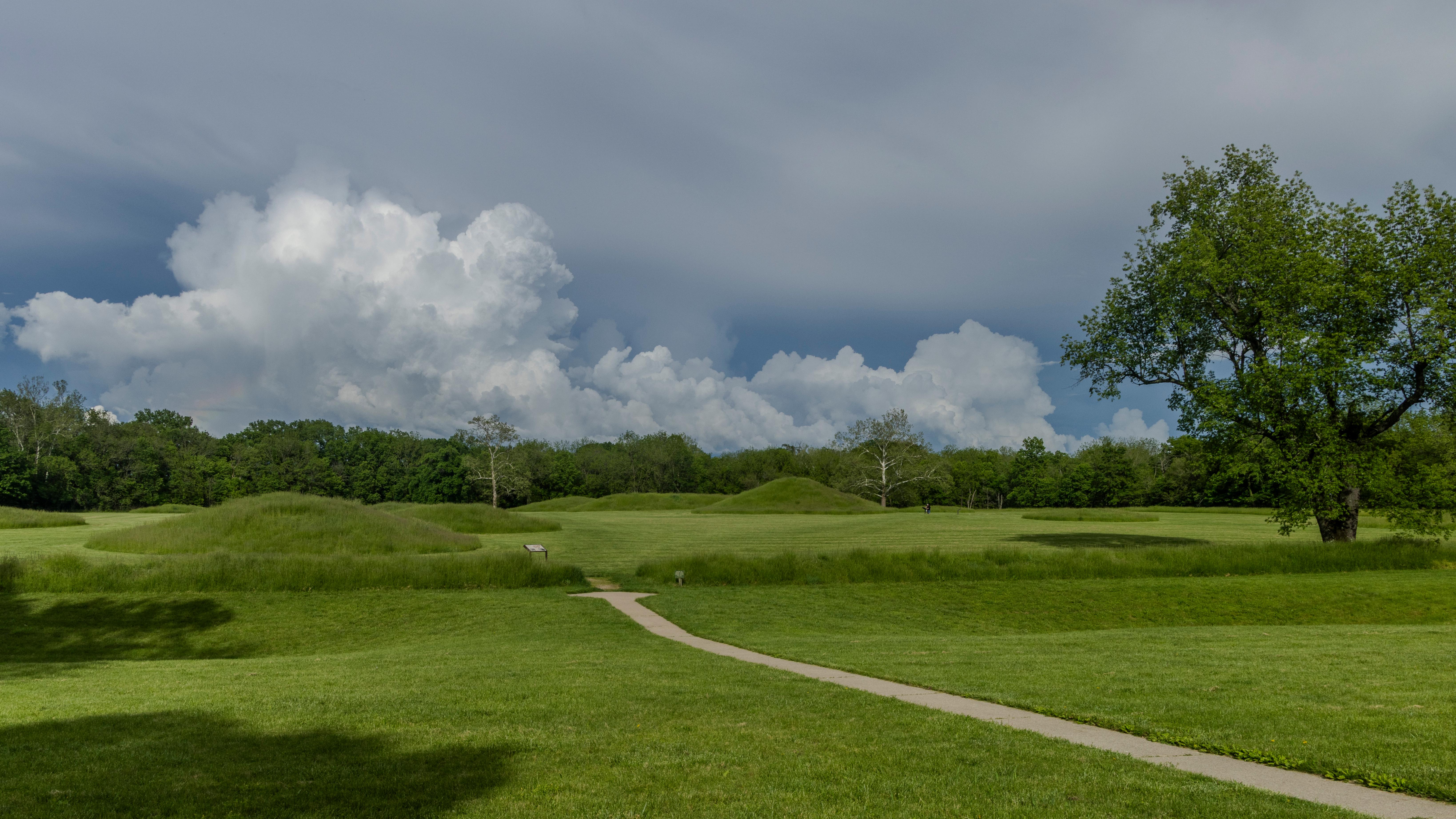 large, green, grass-covered mounds under a blue-gray sky