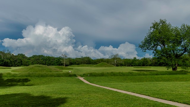 large, green, grass-covered mounds under a blue-gray sky