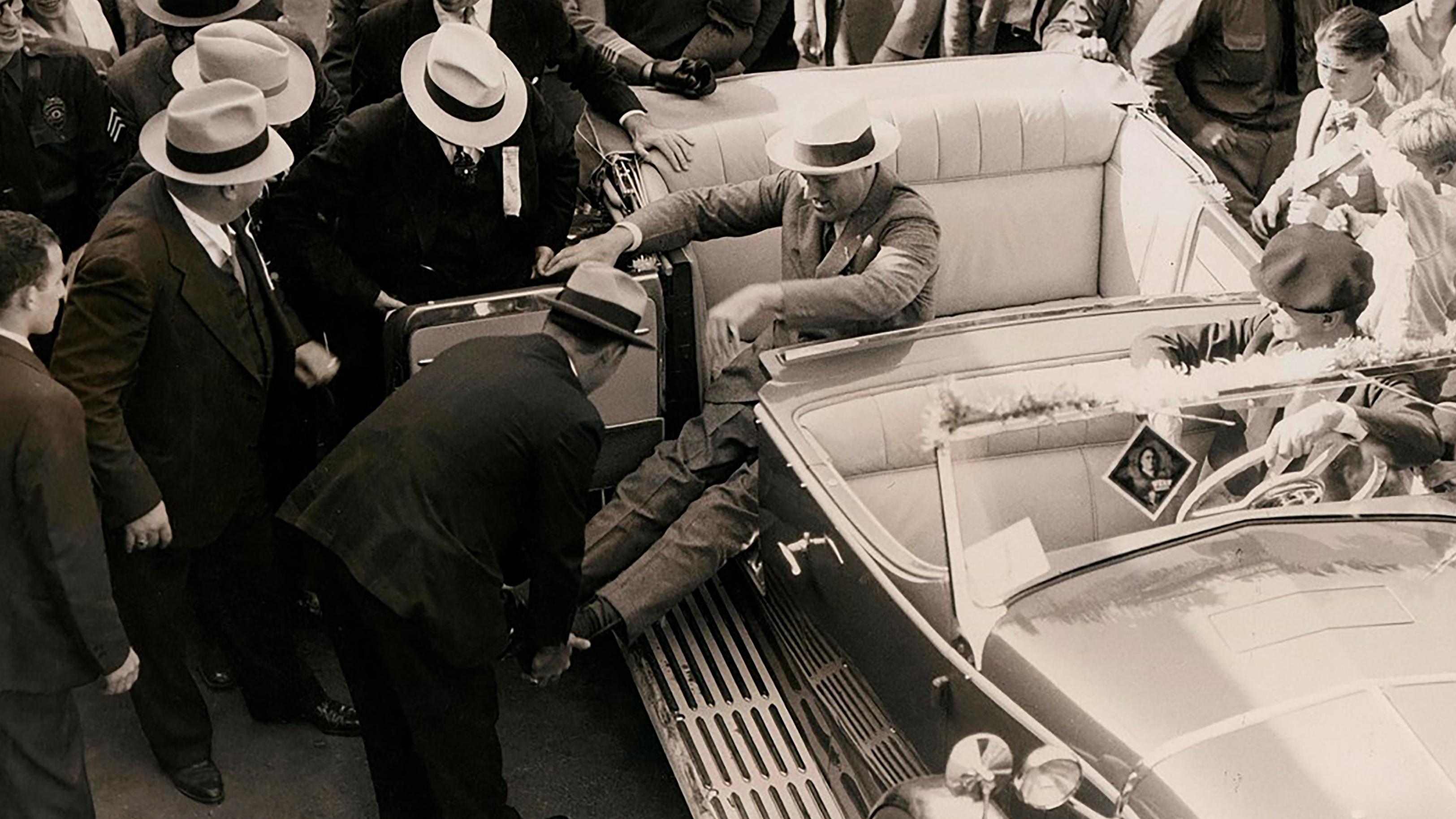 An eager crowd watches as Secret Service agents straighten and lock FDR&rsquo;s leg braces in preparation.