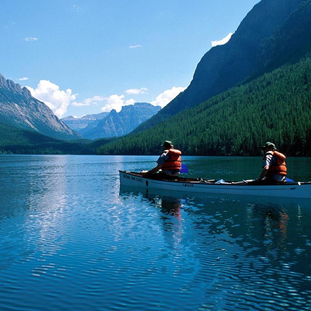 People on a canoe in calm waters surrounded by mountains.